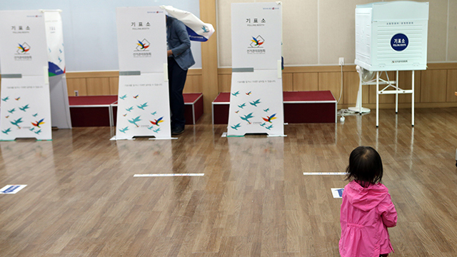 한 아이가 아빠의 투표 모습을 유심히 지켜보고 있다.